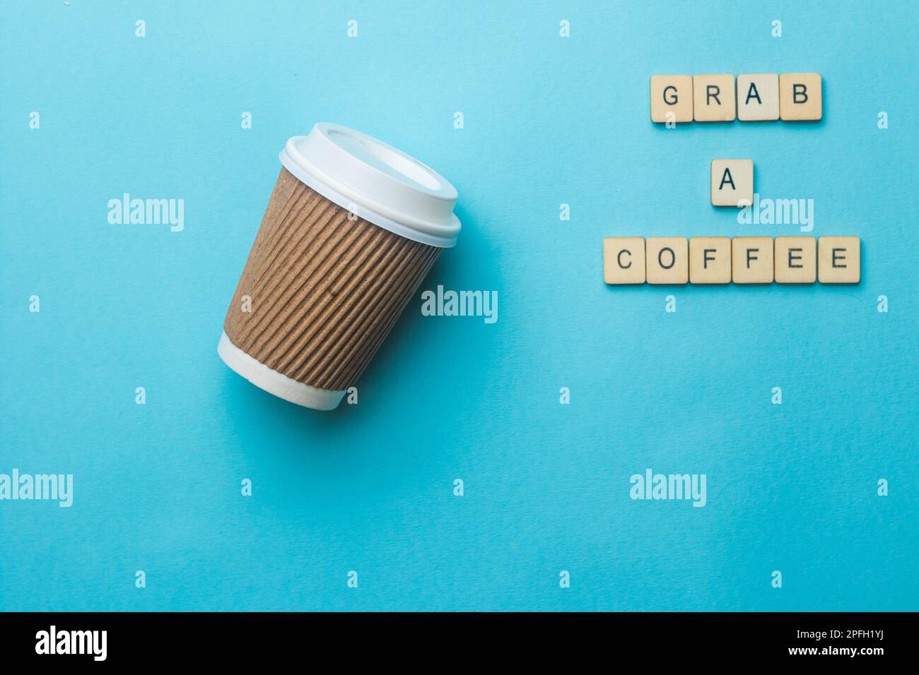 Una tazza da caffè di carta e il coperchio su uno sfondo blu con un segno di lettura afferrare un caffè Foto Stock