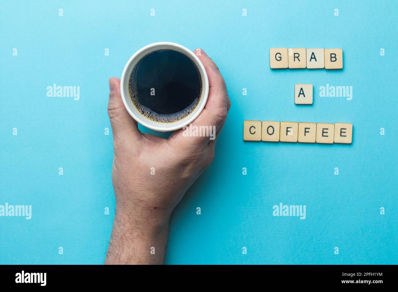Una tazza di carta aperta di caffè nero tenuta da una mano su uno sfondo blu con un segno di lettura afferrare un caffè Foto Stock
