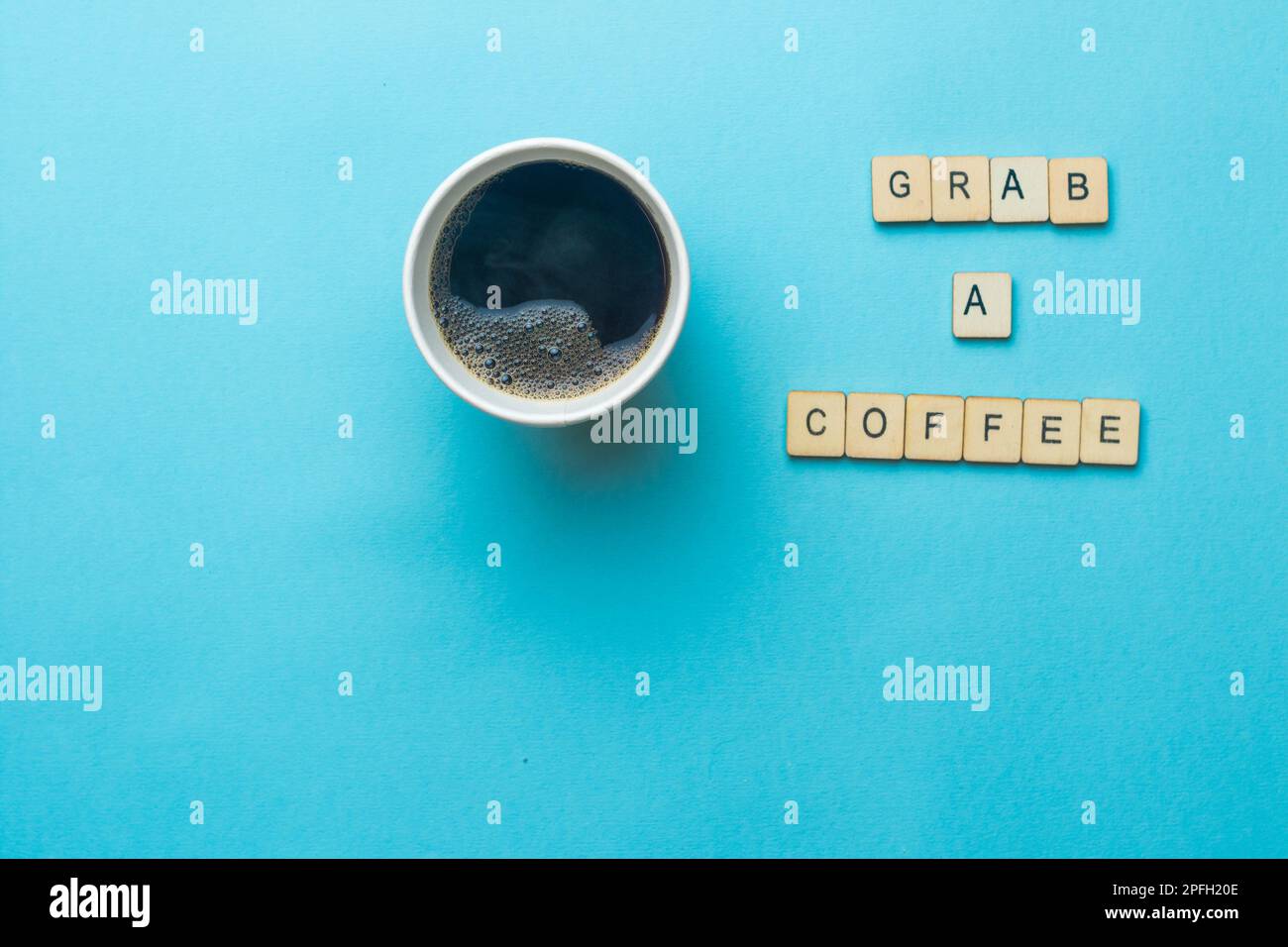 Una tazza di carta aperta di caffè nero su uno sfondo blu con un segno di lettura afferrare un caffè Foto Stock