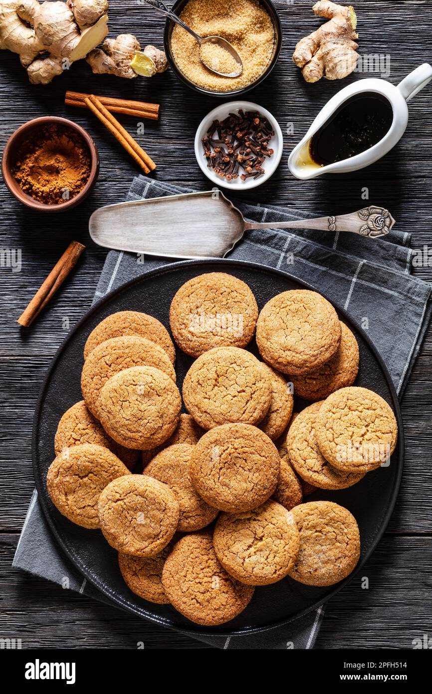 biscotti allo zenzero morbidi su piastra nera su tavolo di rovere scuro con ingredienti, vista verticale dall'alto Foto Stock