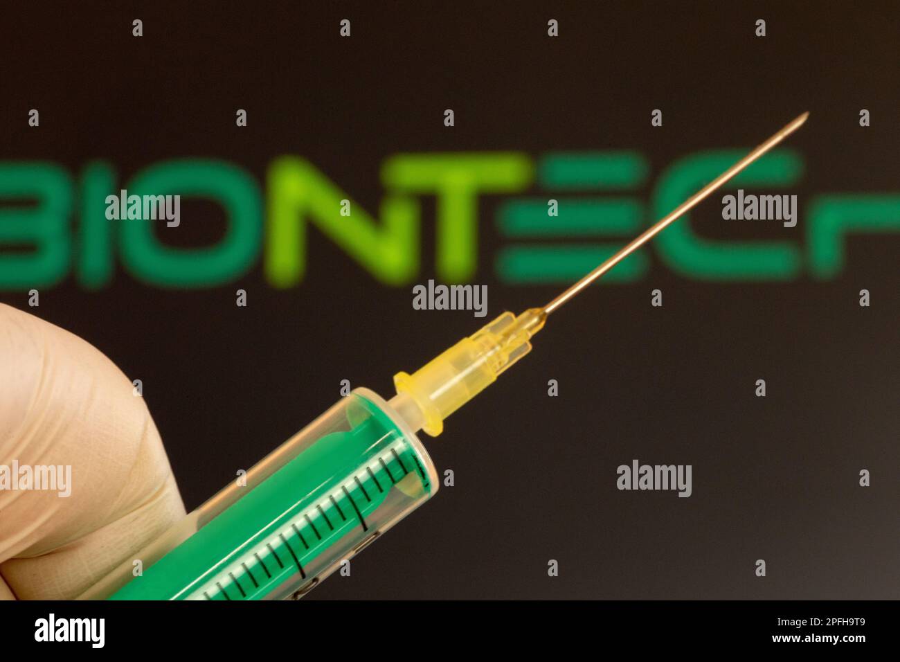 Immagine simbolo vaccinazione a corona/Biontech: Primo piano di un ago ipodermico, logo Biontech sullo sfondo. Il dibattito sul possibile danno da vaccino i Foto Stock