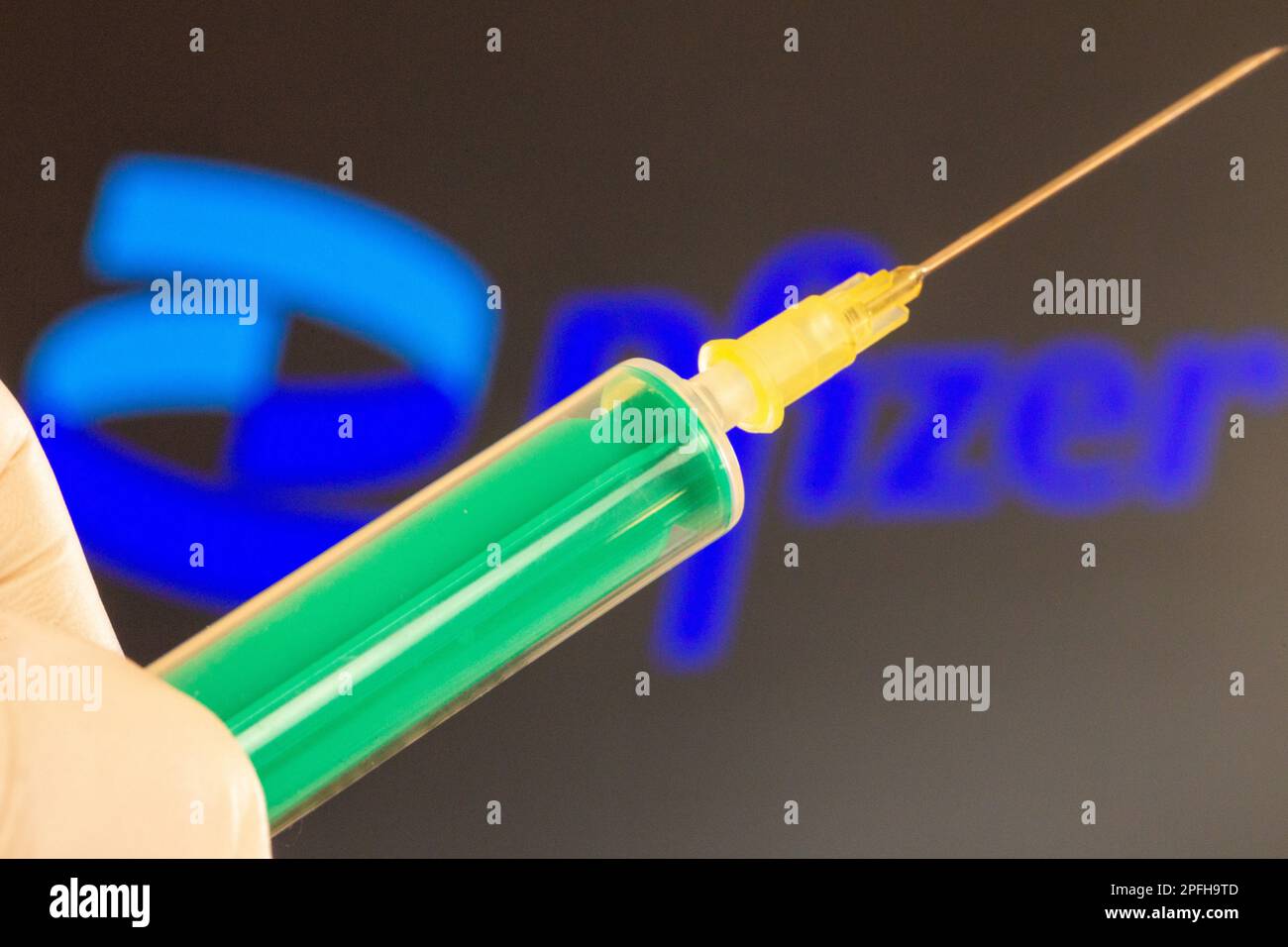 Immagine simbolo vaccinazione a corona/Pfizer: Primo piano di un ago ipodermico, logo Pfizer sullo sfondo. Il dibattito su possibili danni da vaccino è cu Foto Stock