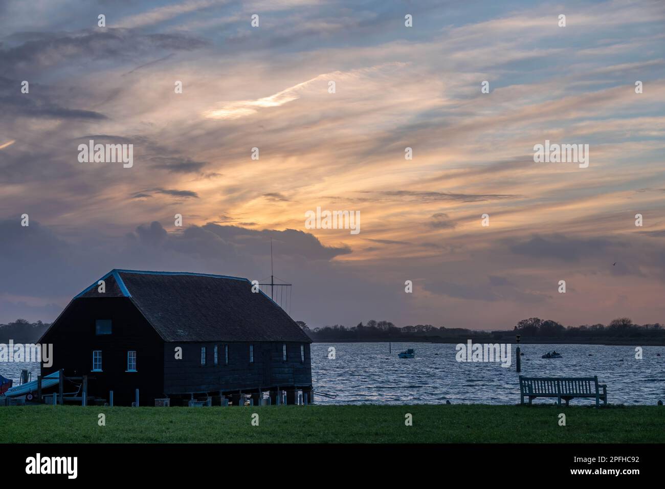 Raptackle capanna di legno Bosham West Sussex Inghilterra come il sole tramonta con un cielo nuvoloso blu e arancione sullo sfondo Foto Stock