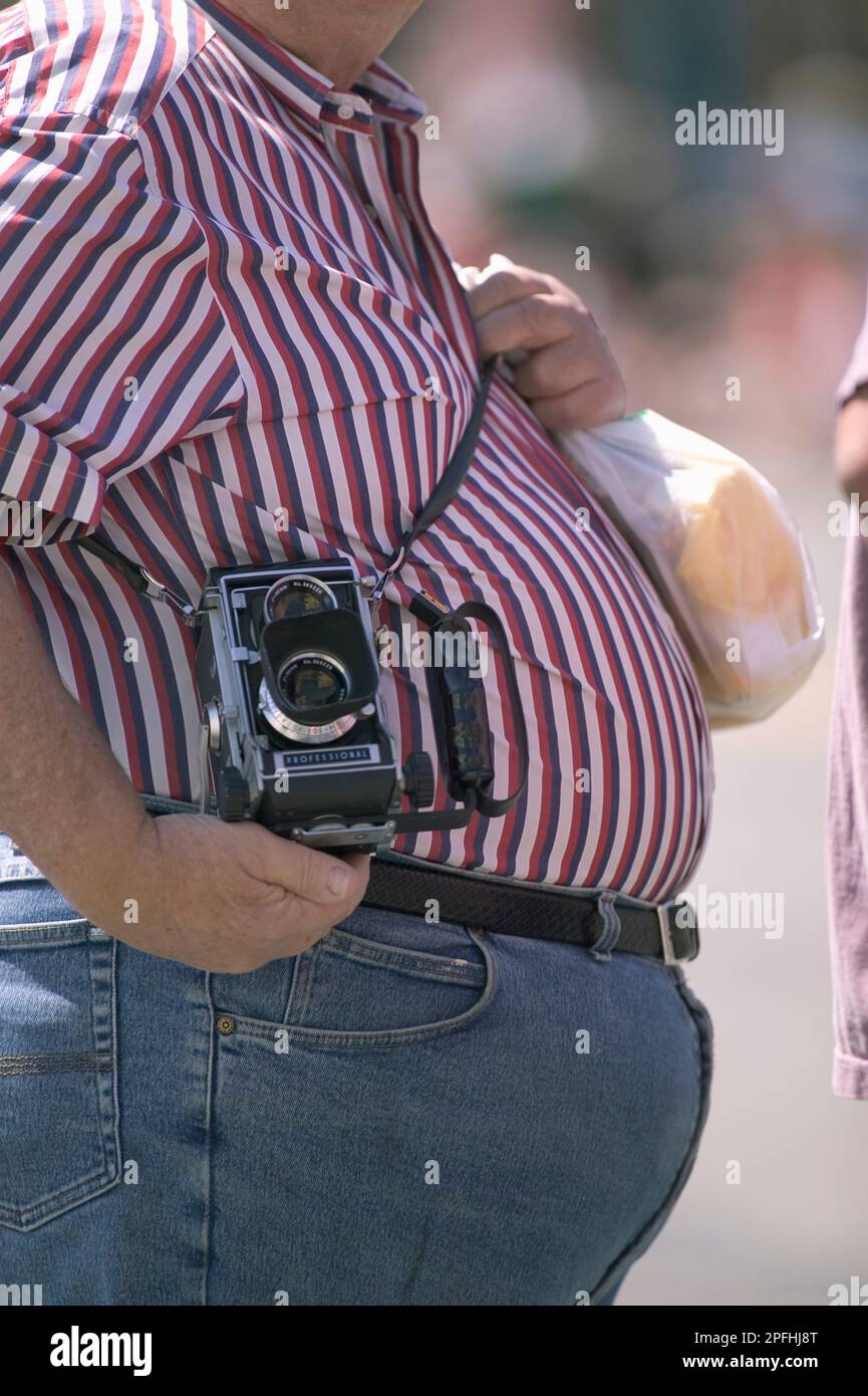 Un appassionato di fotocamera sovrappeso che indossa una tracolla retrò alla sua spalla Foto Stock