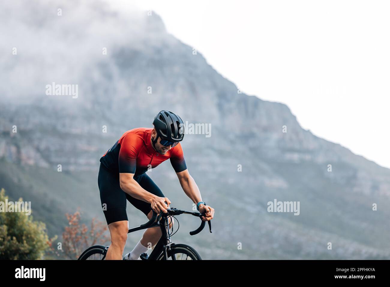 Un pilota professionista in bicicletta che fa un intenso allenamento all'aperto contro la montagna con le nuvole Foto Stock