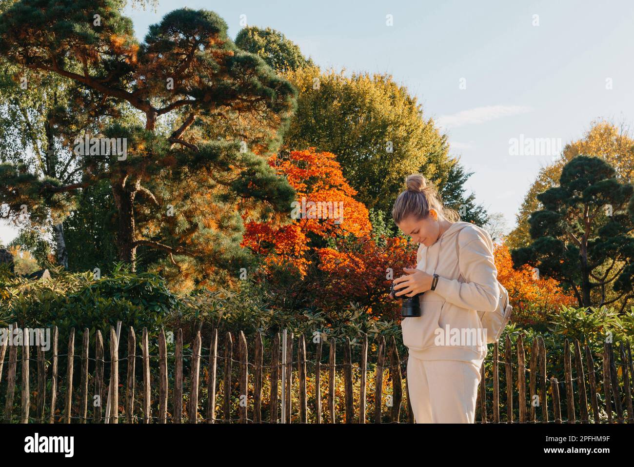 Bella giovane donna scatta foto con una fotocamera professionale nella foresta autunnale. Ragazza sorridente che si gode il tempo autunnale. Riposo, relax, stile di vita conc Foto Stock