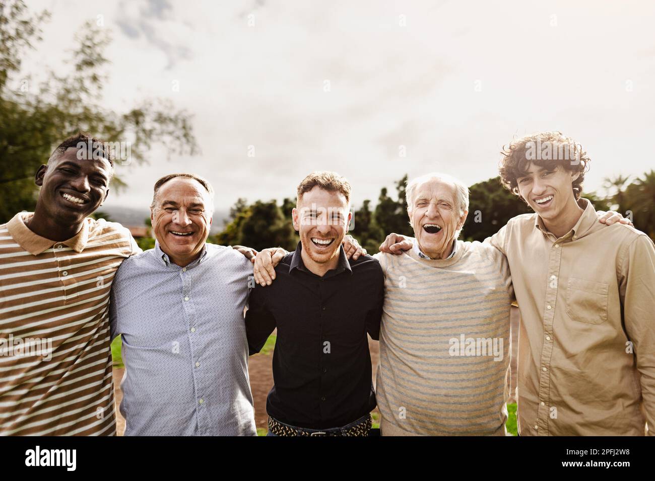 Felice gruppo multigenerazionale di uomini con diverse età ed etnie che si divertono sorridendo davanti alla macchina fotografica al parco Foto Stock