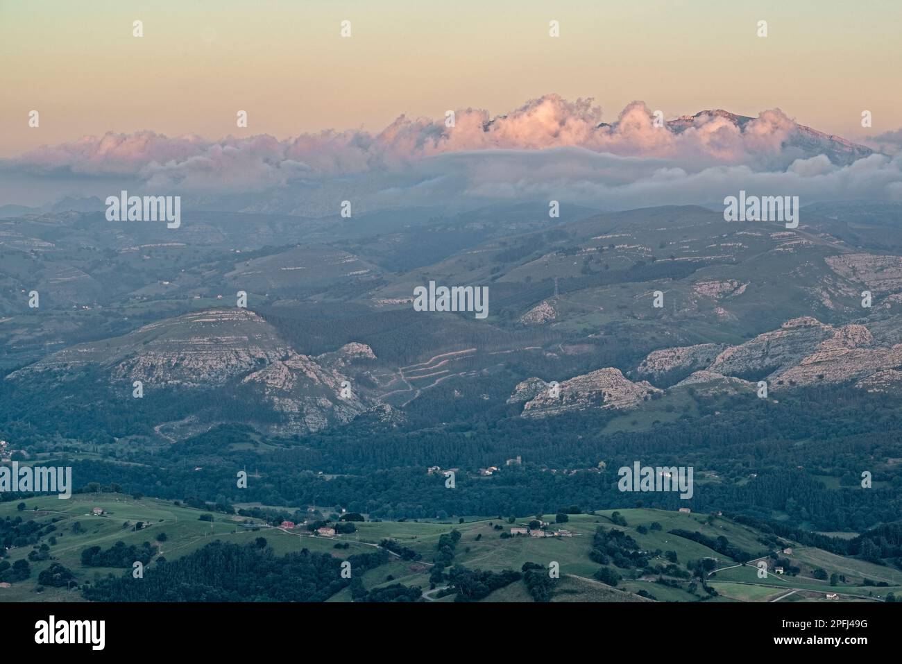 Vista aerea della valle e delle montagne della catena montuosa della Cantabria con alcune fitte nuvole arroccate su di essa in un tramonto visto da Peña Cabarga, Foto Stock