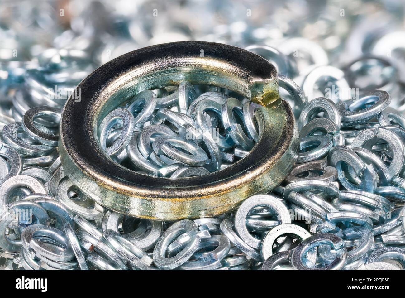 Rondella elastica in metallo grande giacente su un mucchio di piccole rondelle spaccate in acciaio inossidabile sfocate sullo sfondo. Primo piano dell'anello elicoidale in acciaio per il fissaggio a vite e dado. Foto Stock