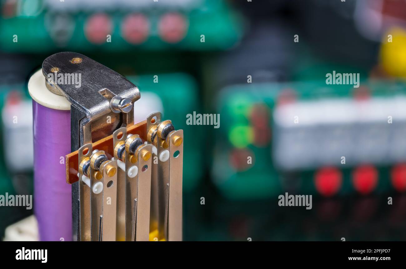 Relè elettromeccanico di potenza e componenti elettronici sfocati su sfondo colorato. Bobina elettromagnetica viola e serie di contatti mobili di un interruttore. Foto Stock