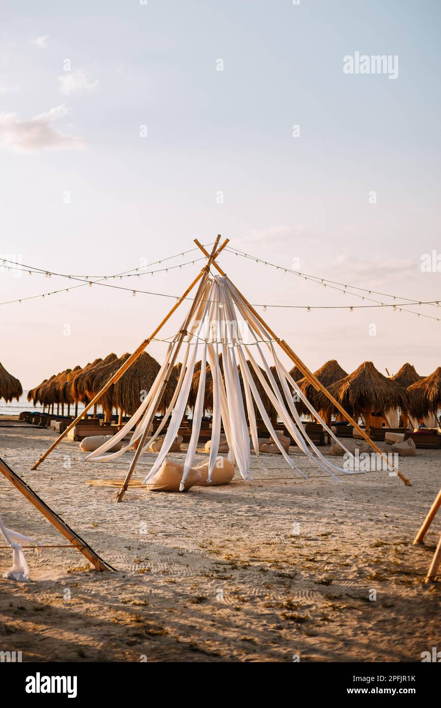 Boho tenda e cuscini sulla spiaggia, alla luce del tramonto. Tessuto bianco sospeso dalla parte superiore della tenda Foto Stock