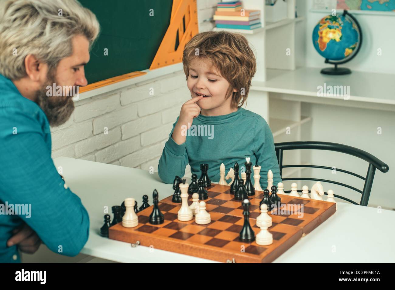 Carino bambino giocare a scacchi con padre. Bell'insegnante che dà lezioni private di scacchi al ragazzo prescolare. Ritorno a scuola. Felice Padre e figlio. Foto Stock