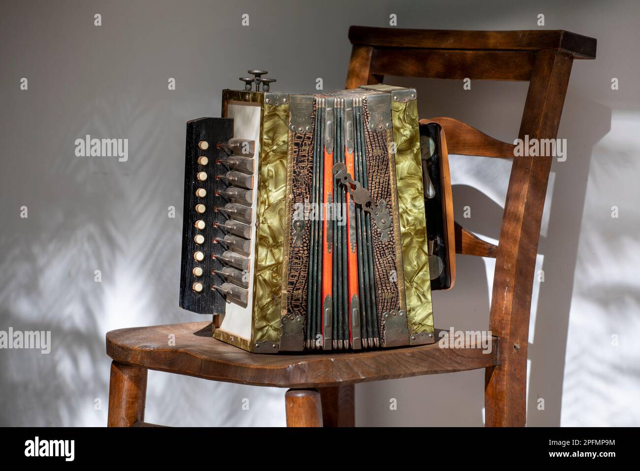 Vintage Gebrüder Ludwig, fisarmonica a bottoni su sedia di legno, all'esterno con ombre, primo piano. Foto Stock