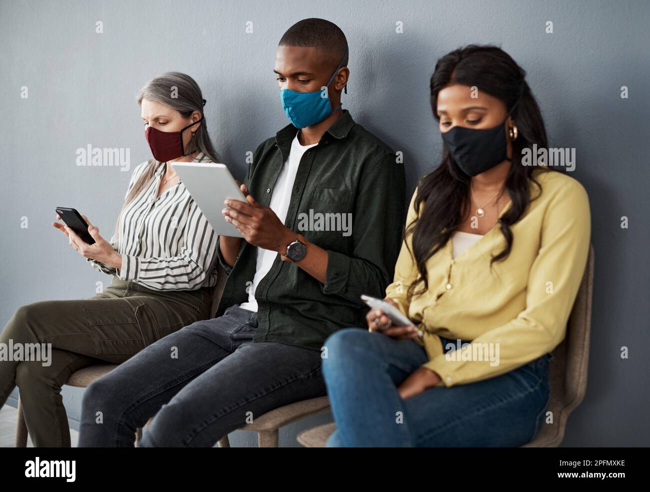 Dio benedica la luce del giorno. un gruppo cauto di persone che si allontanano socialmente mentre utilizzano i loro dispositivi intelligenti contro una parete grigia. Foto Stock