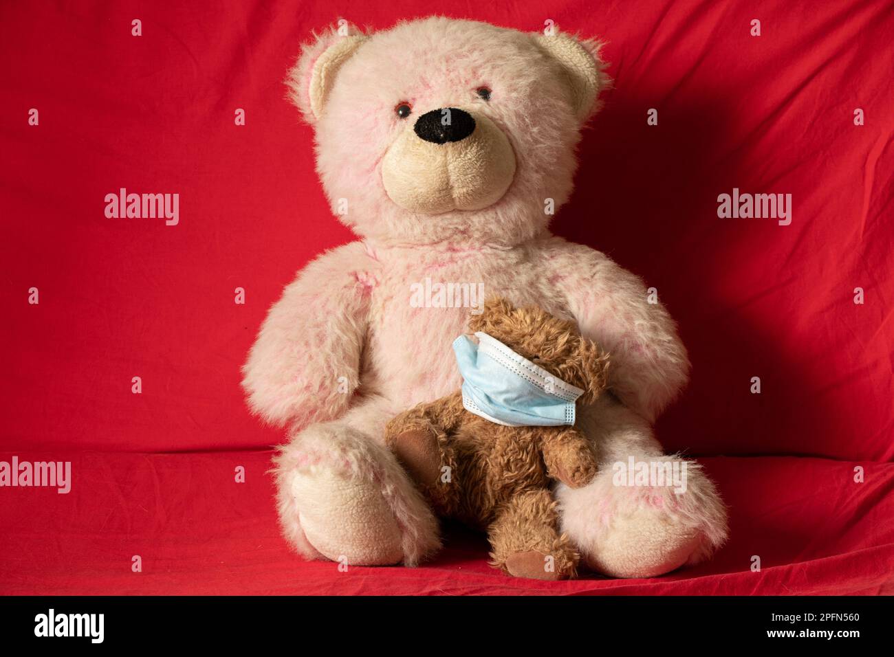 i giocattoli morbidi di peluche per bambini in maschera medica giacciono sul divano rosso, sulla salute e sulla medicina, sulla morbilità dei bambini Foto Stock