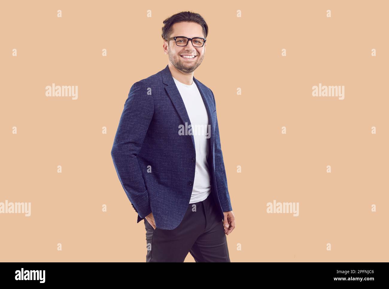 Bruna sorridente uomo d'affari fiducioso in giacca blu con mano in tasca su sfondo beige. Foto Stock