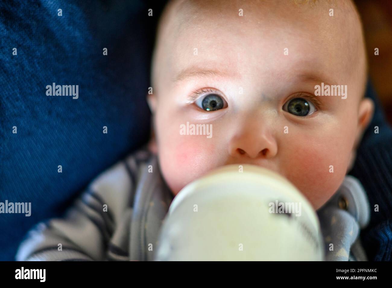 Bambino che beve latte da un biberon, primo piano, occhi blu Foto Stock