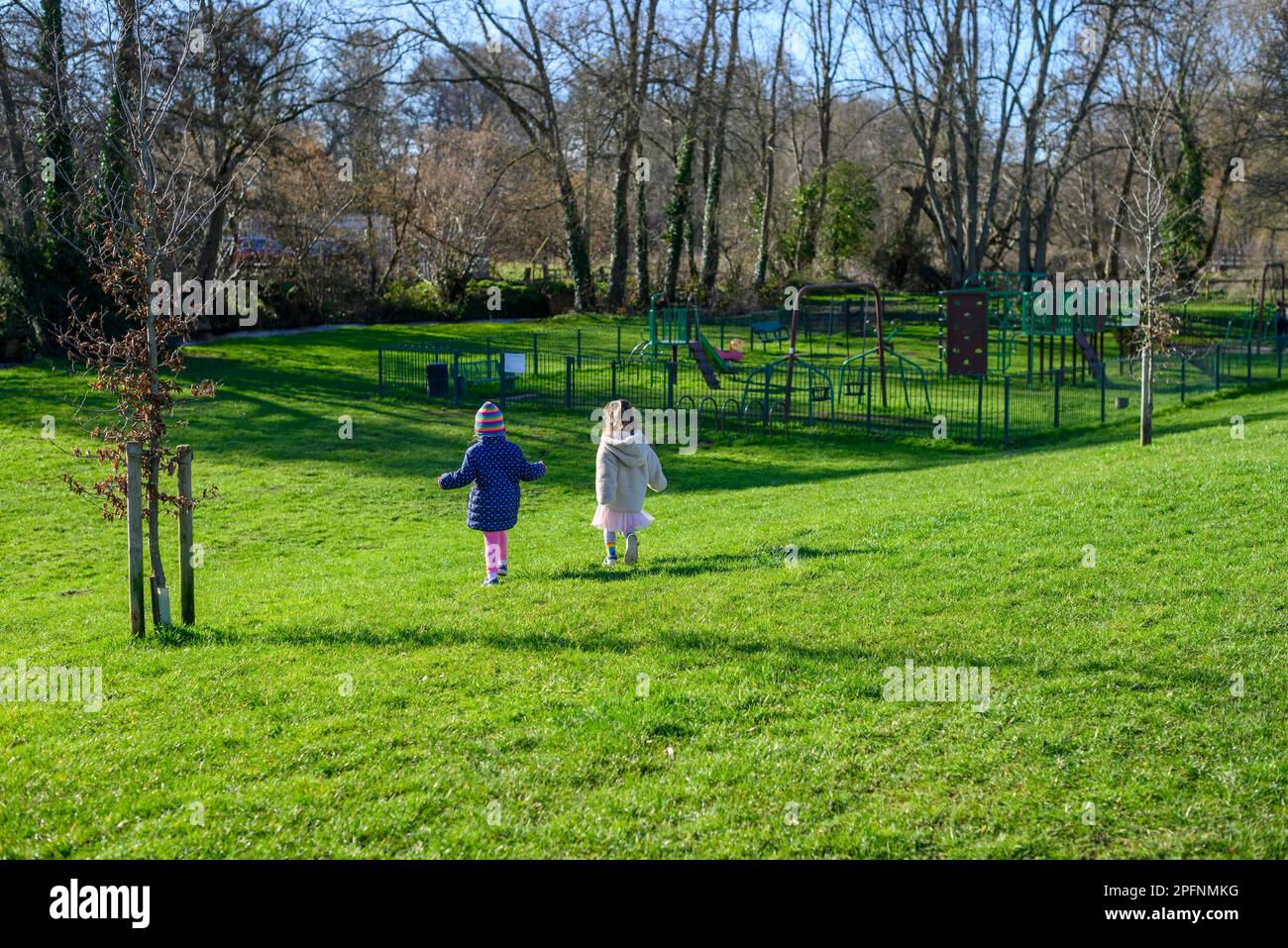 I bambini corrono attraverso l'erba verde verso un parco giochi Foto Stock