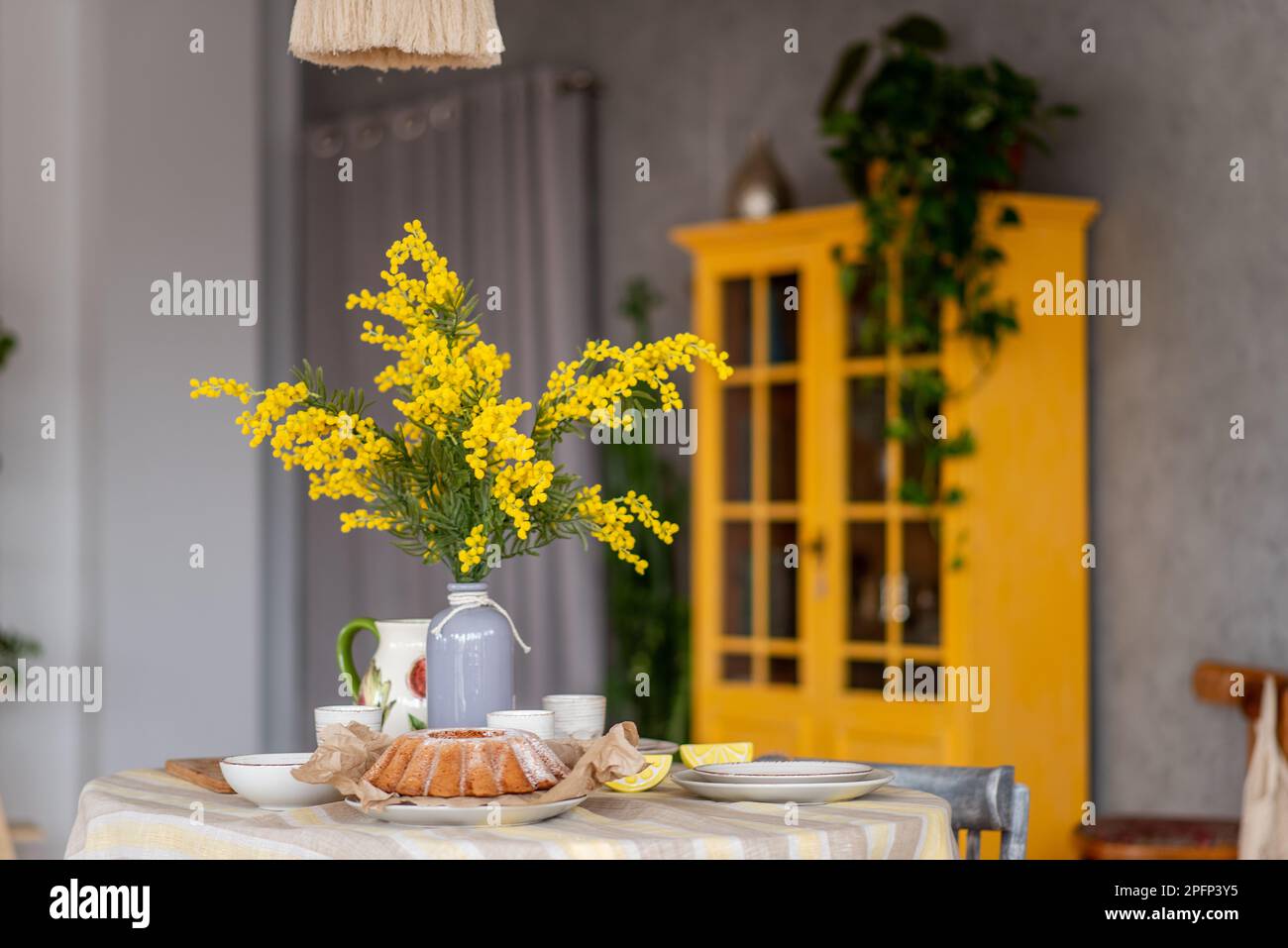 Primavera, Pasqua interni in stile scandinavo. Rustico soggiorno con un luminoso armadio, mimosa giallo in vaso. La tabella viene impostata in modo festivo con ceram Foto Stock