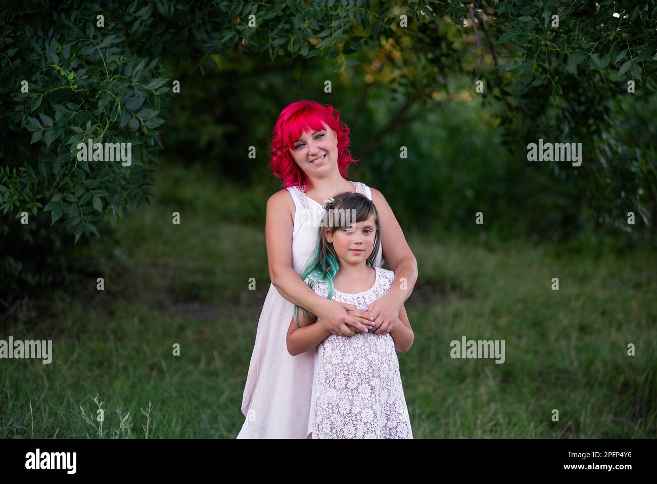 Luminosa, diversità, straordinaria madre e figlia che abbraccia la foresta. La donna ha i capelli rosa, la ragazza ha i capelli verdi. Tenera maternità, buon chi Foto Stock