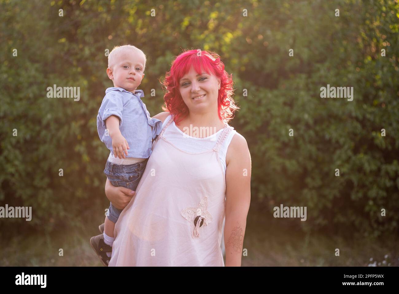 Ritratto di luce, diversità, straordinaria madre e figlio piccolo abbracciare nella foresta. Donna ha capelli rosa. Tenera maternità, felice infanzia. Ris Foto Stock