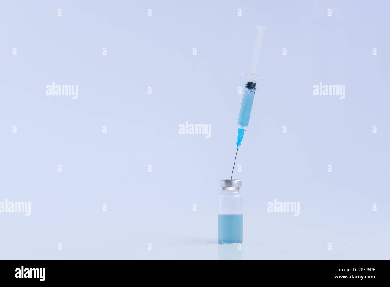 Su sfondo bianco isolato, flaconcino di vetro trasparente con vaccino blu contro i virus con siringa monouso. Lotta contro le epidemie di infezione. Co Foto Stock