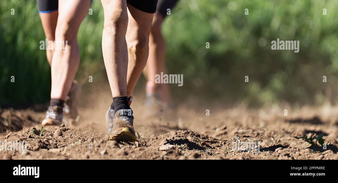 Atlete trail running che si allenano per il fitness e la salute all'aperto arato campo, primo piano di scarpe da running in azione Foto Stock