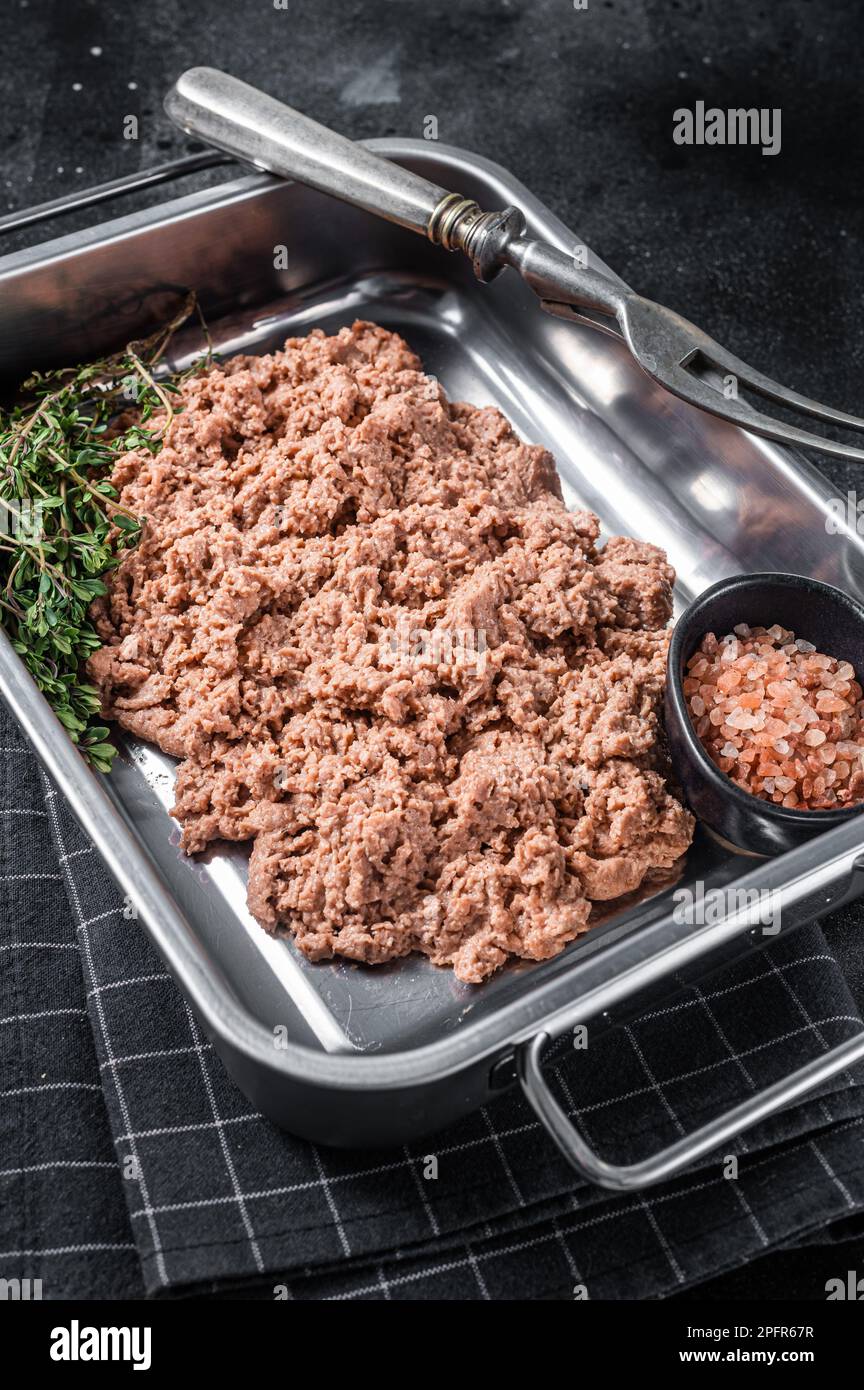 Carne macinata vegetariana, carne a base di piante crude con erbe aromatiche nel vassoio della cucina Sfondo nero. Vista dall'alto. Foto Stock
