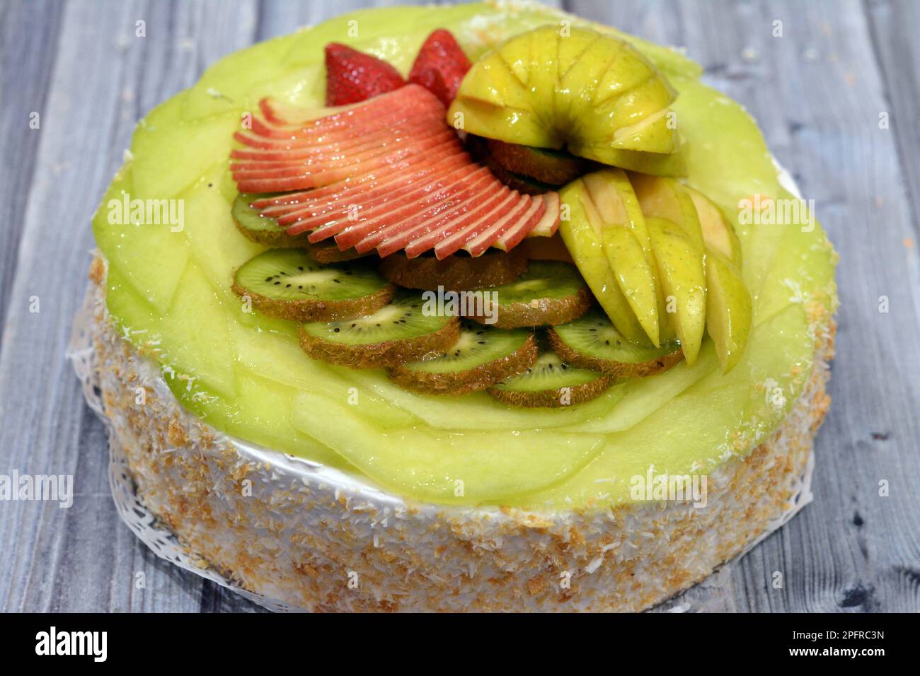 Una pan di Spagna di frutta fresca ricoperta e farcita con panna montata e noci grattugiate e ricoperta con frutta fresca di stagione con fette di AP verde e rosso Foto Stock