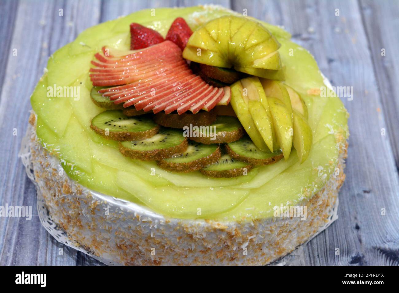 Una pan di Spagna di frutta fresca ricoperta e farcita con panna montata e noci grattugiate e ricoperta con frutta fresca di stagione con fette di AP verde e rosso Foto Stock