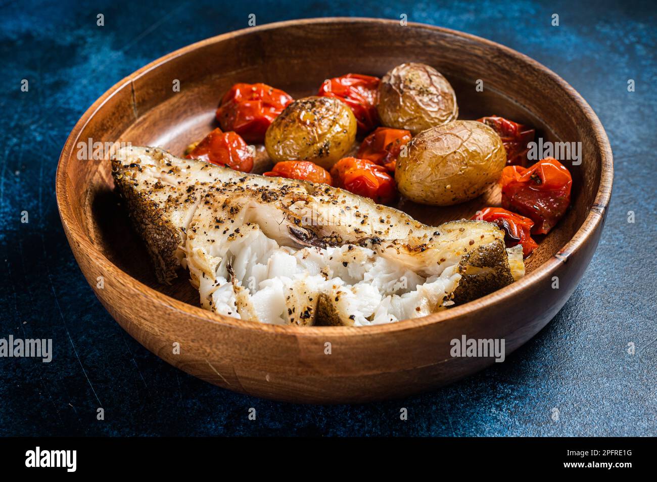 Pesce halibut al forno con pomodoro arrosto e patate in piatto di legno.  Sfondo blu. Vista dall'alto. Spazio di copia Foto stock - Alamy