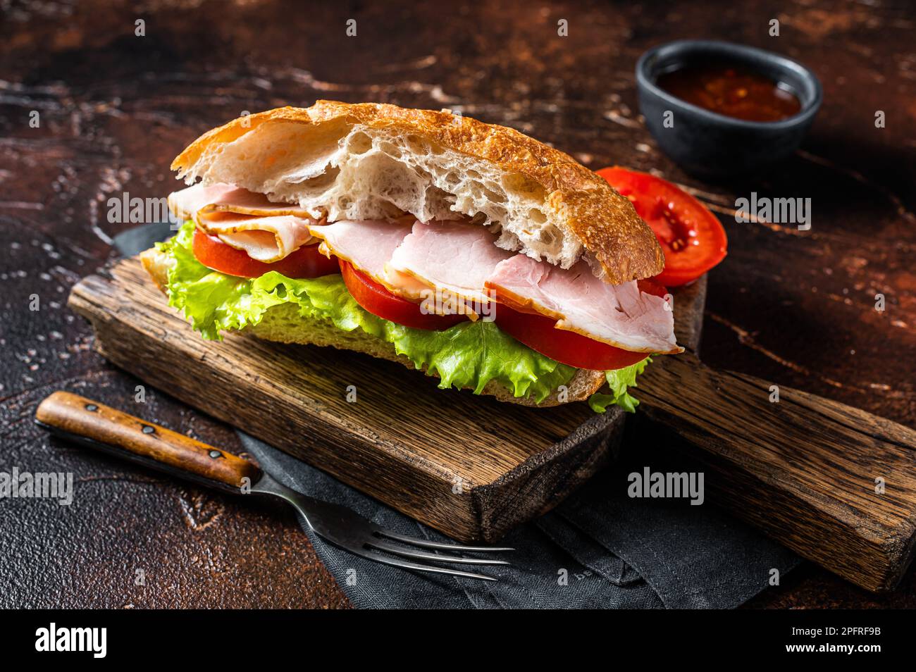 Panino di tacchino affumicato con prosciutto, formaggio, pomodoro e lattuga. Sfondo scuro. Vista dall'alto. Foto Stock