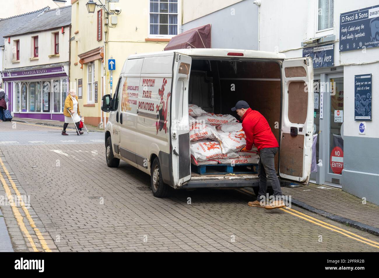 Consegna autista che scarica sacchi di patate in un negozio locale di pesce e patatine a Tenby Pembrokeshire Foto Stock