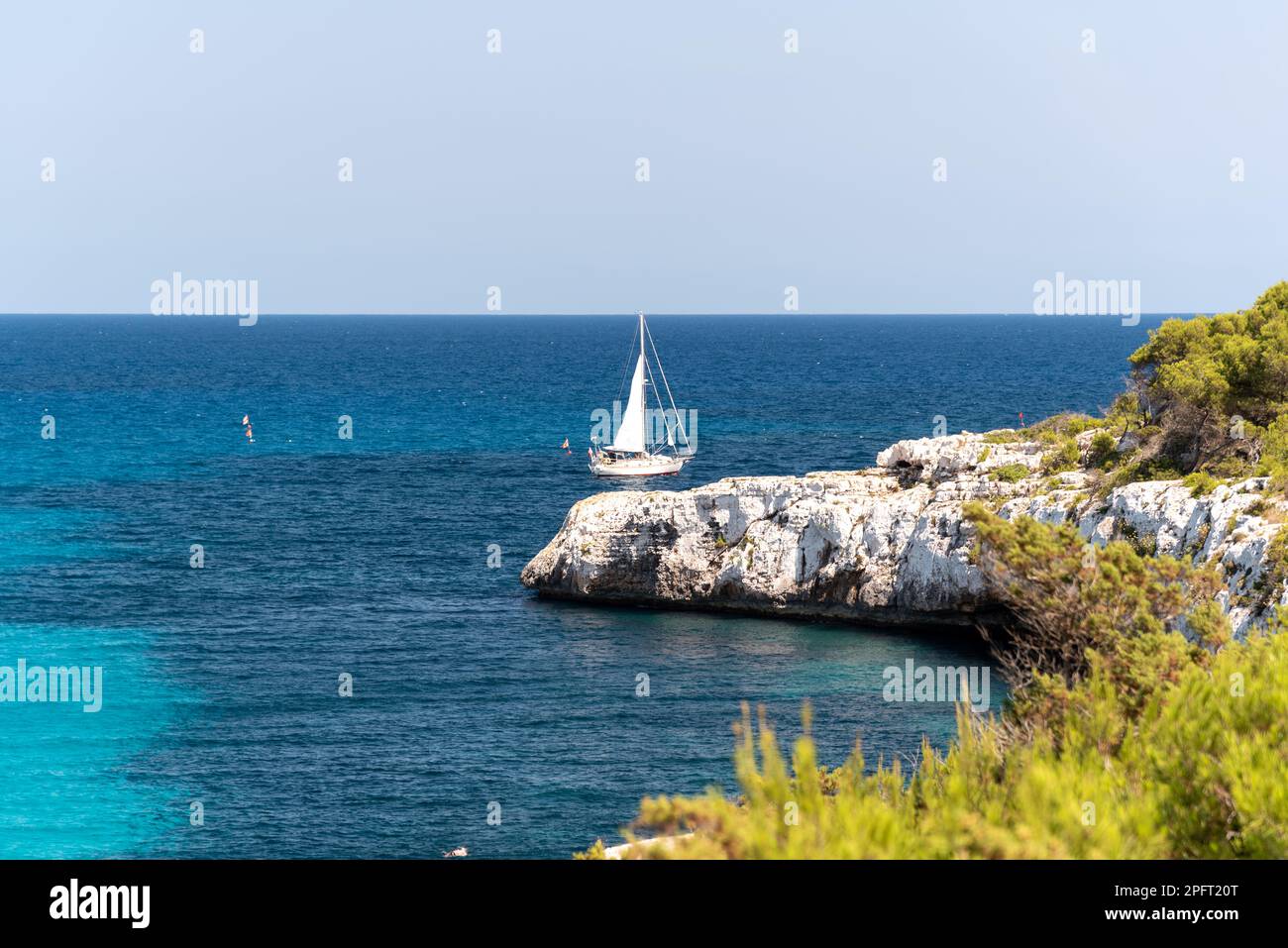 A Cala Llombards a Mallorca, Spagna, le acque tranquille del Mediterraneo incontrano una spiaggia di sabbia bianca incontaminata, con barche che si libricano dolcemente sulla hor Foto Stock