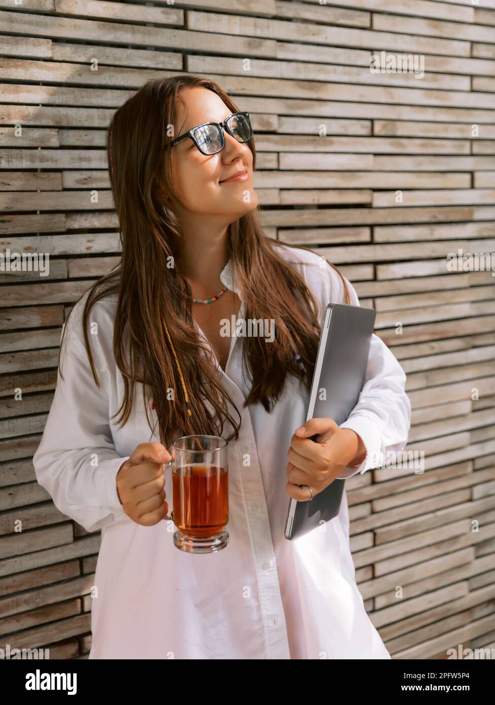 Giovane donna freelancer con bicchieri e tenendo un computer portatile con una tazza di tè Foto Stock