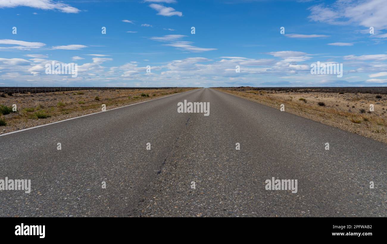 Una lunga strada diritta senza linee che attraversa il deserto di Atacama in Cile. Sole con nuvole nel cielo blu. Foto Stock