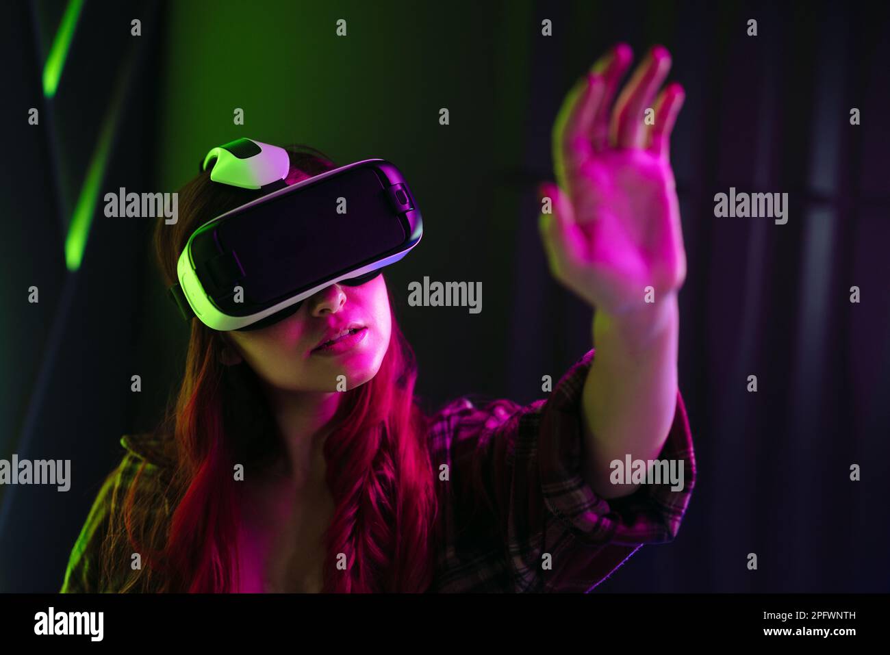 Donna che si sta allungando la mano per toccare gli oggetti nella realtà virtuale, interagendo con il mondo simulato creato da un visore VR. Giovane donna esplorante Foto Stock