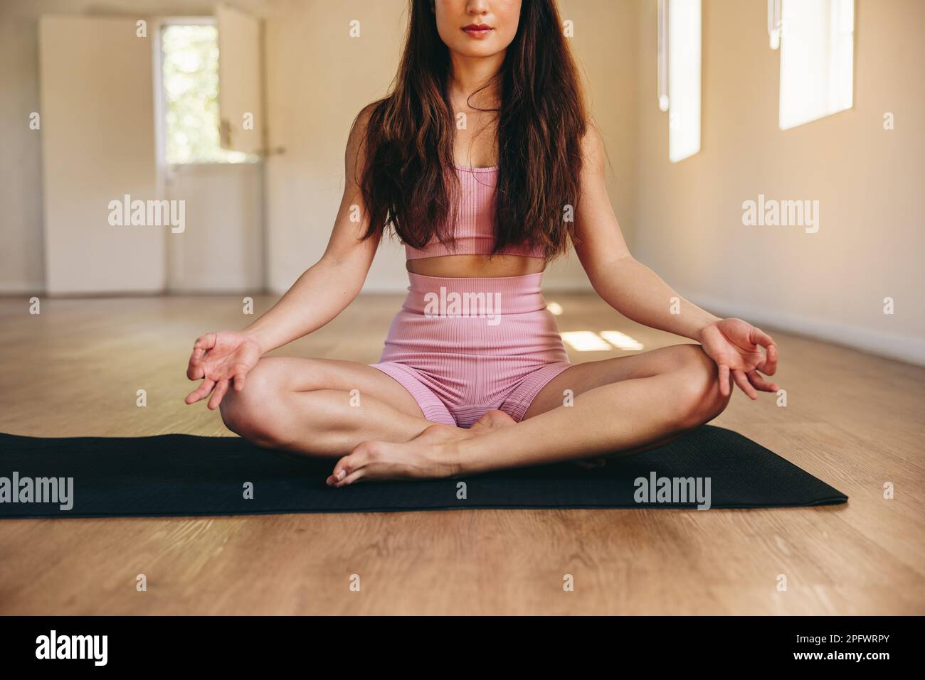 Giovane donna medita mentre si siede in posa facile in uno studio di yoga. Adatta la giovane donna che pratica un esercizio di respirazione e relax su un tappetino yoga. Foto Stock