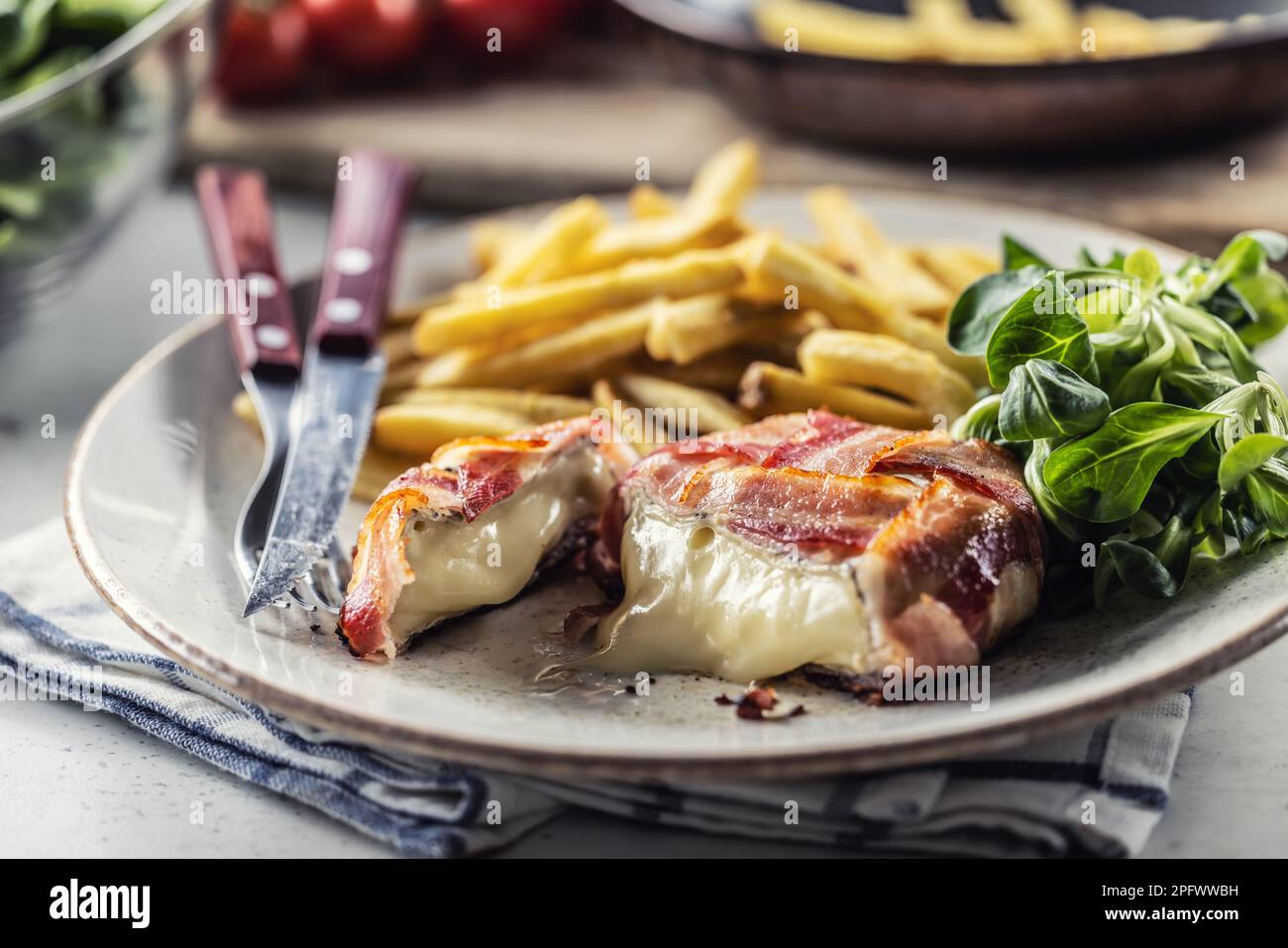 Tagliare il formaggio in un involucro di pancetta servito su un piatto con patatine fritte e insalata verde. Foto Stock