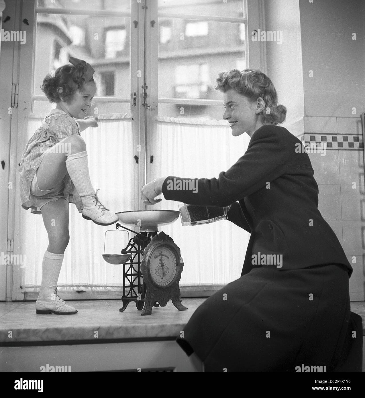 Scarpe negli anni '1940s. Una madre con la figlia accanto alla finestra. Mentre sta misurando qualcosa su una scala la ragazza mostra le sue scarpe. Svezia 1943 Kristoffersson Ref D57-4 Foto Stock