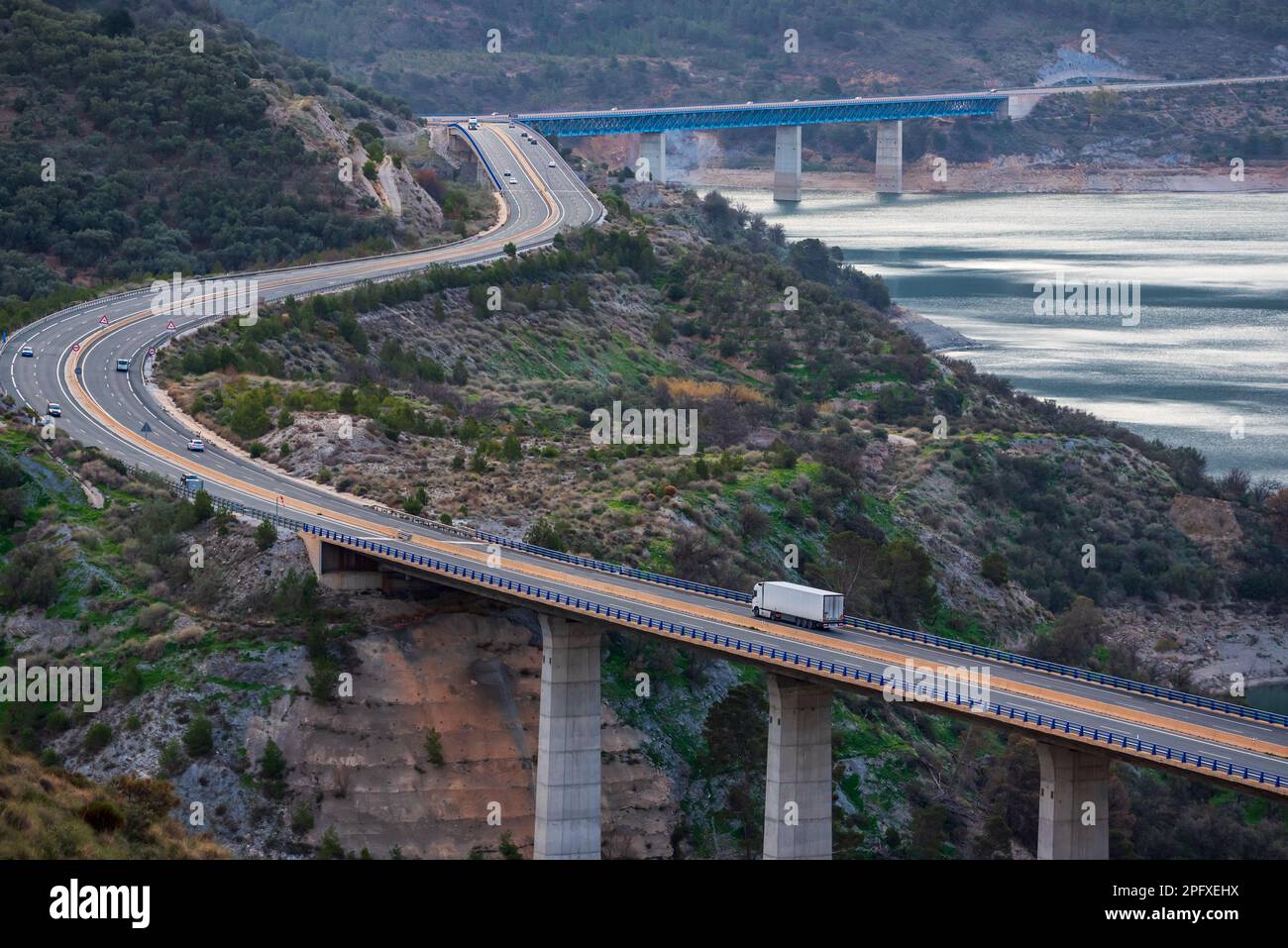 Camion refrigerato che guida su un'autostrada con ponti su una palude, paesaggio stradale in montagna. Foto Stock