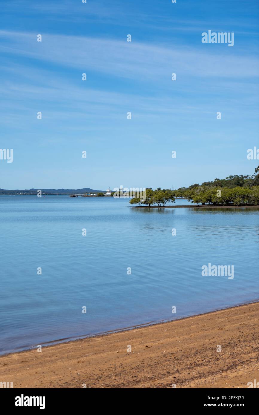 Vista dalla spiaggia di Redland Bay attraverso le belle e tranquille acque di Moreton Bay con il traghetto veicolare in lontananza e le isole all'orizzonte Foto Stock