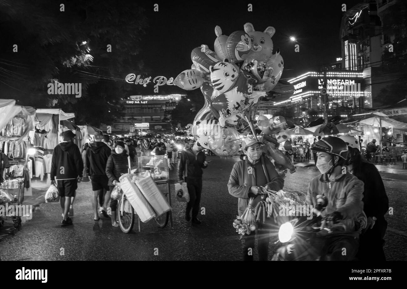 Un venditore di mongolfiere cammina attraverso l'affollato e vivace mercato notturno a Dalat, Vietnam. Foto Stock