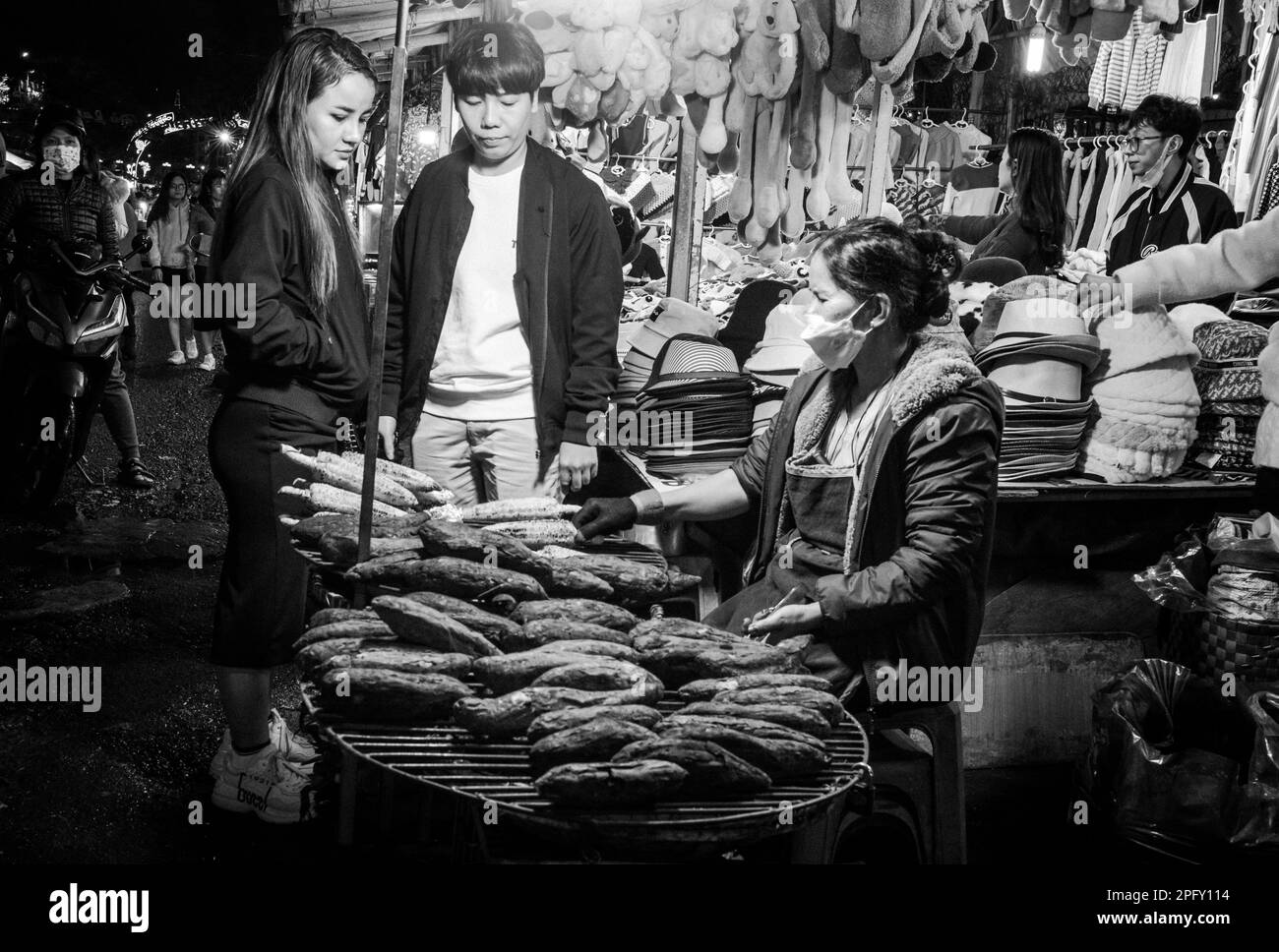 Una giovane coppia vietnamita si ferma per acquistare mais alla griglia al vivace mercato notturno di Dalat, Vietnam. Foto Stock