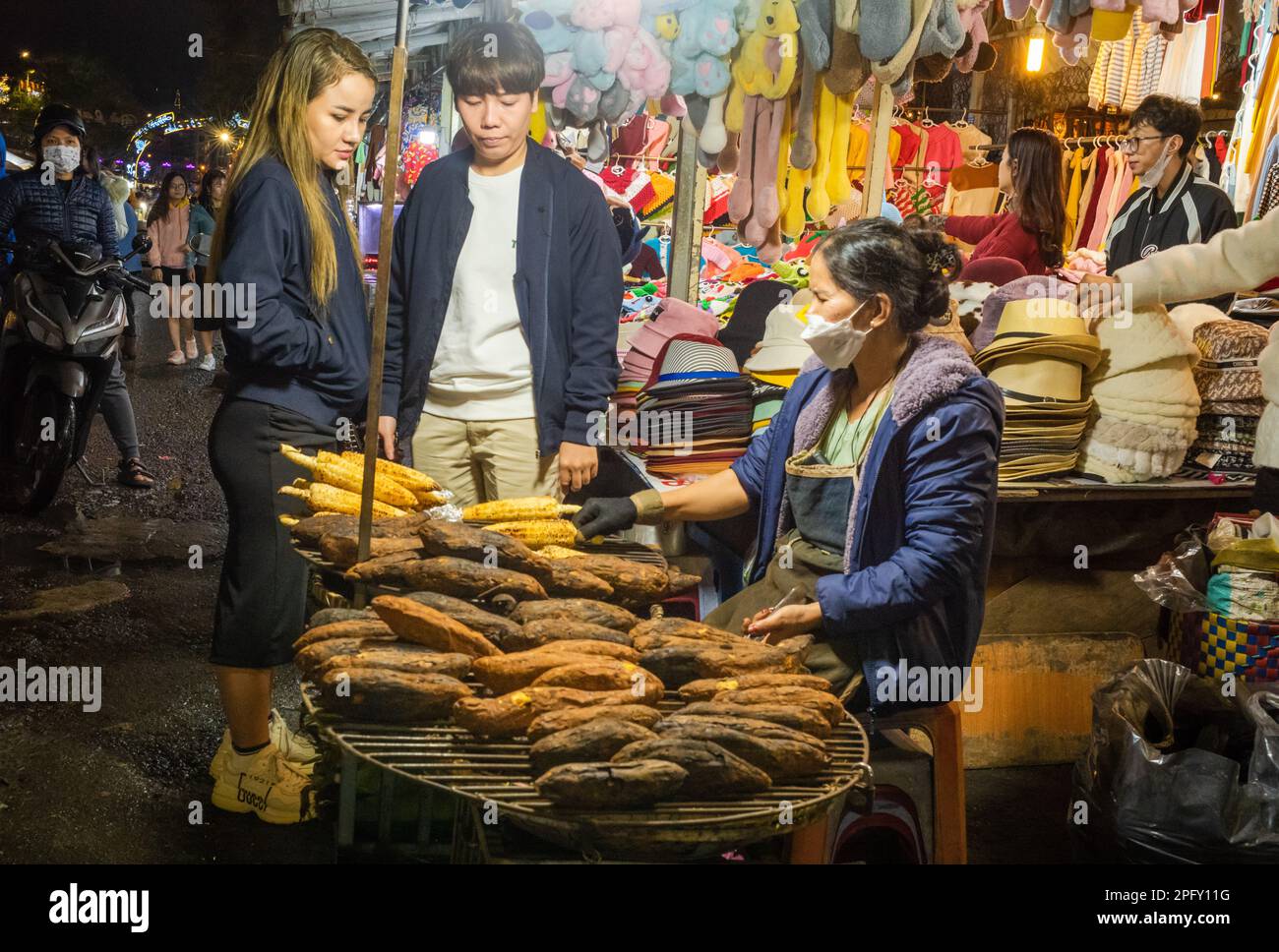 Una giovane coppia vietnamita si ferma per acquistare mais alla griglia al vivace mercato notturno di Dalat, Vietnam. Foto Stock