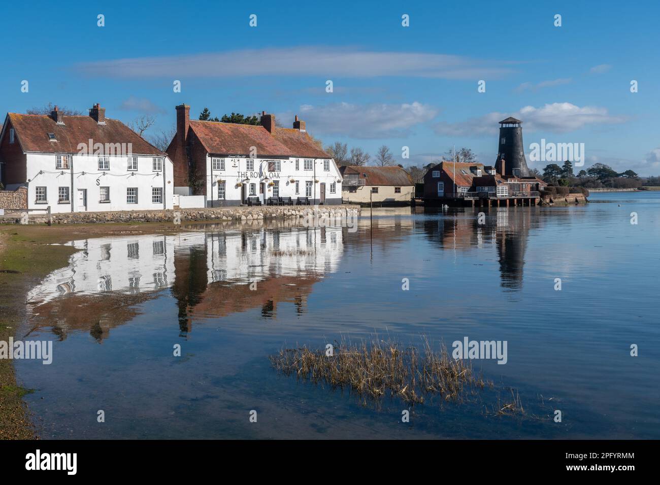 Langstone Harbour, vista del villaggio, vecchio mulino e Royal Oak Pub sul lungomare, Langstone, Hampshire, Inghilterra, Regno Unito, in una giornata di sole Foto Stock