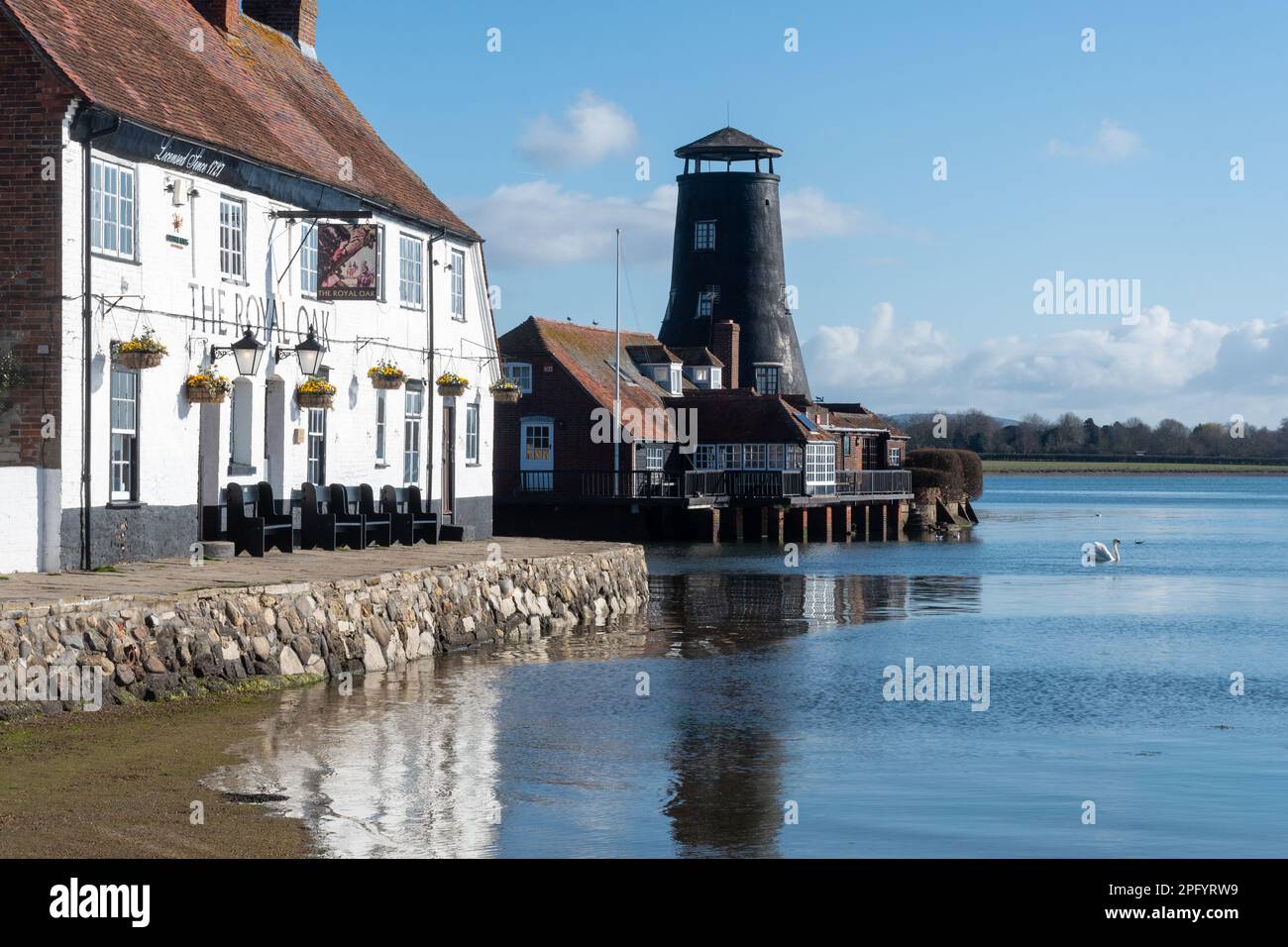 Langstone Harbour, vista del villaggio, vecchio mulino e Royal Oak Pub sul lungomare, Langstone, Hampshire, Inghilterra, Regno Unito, in una giornata di sole Foto Stock