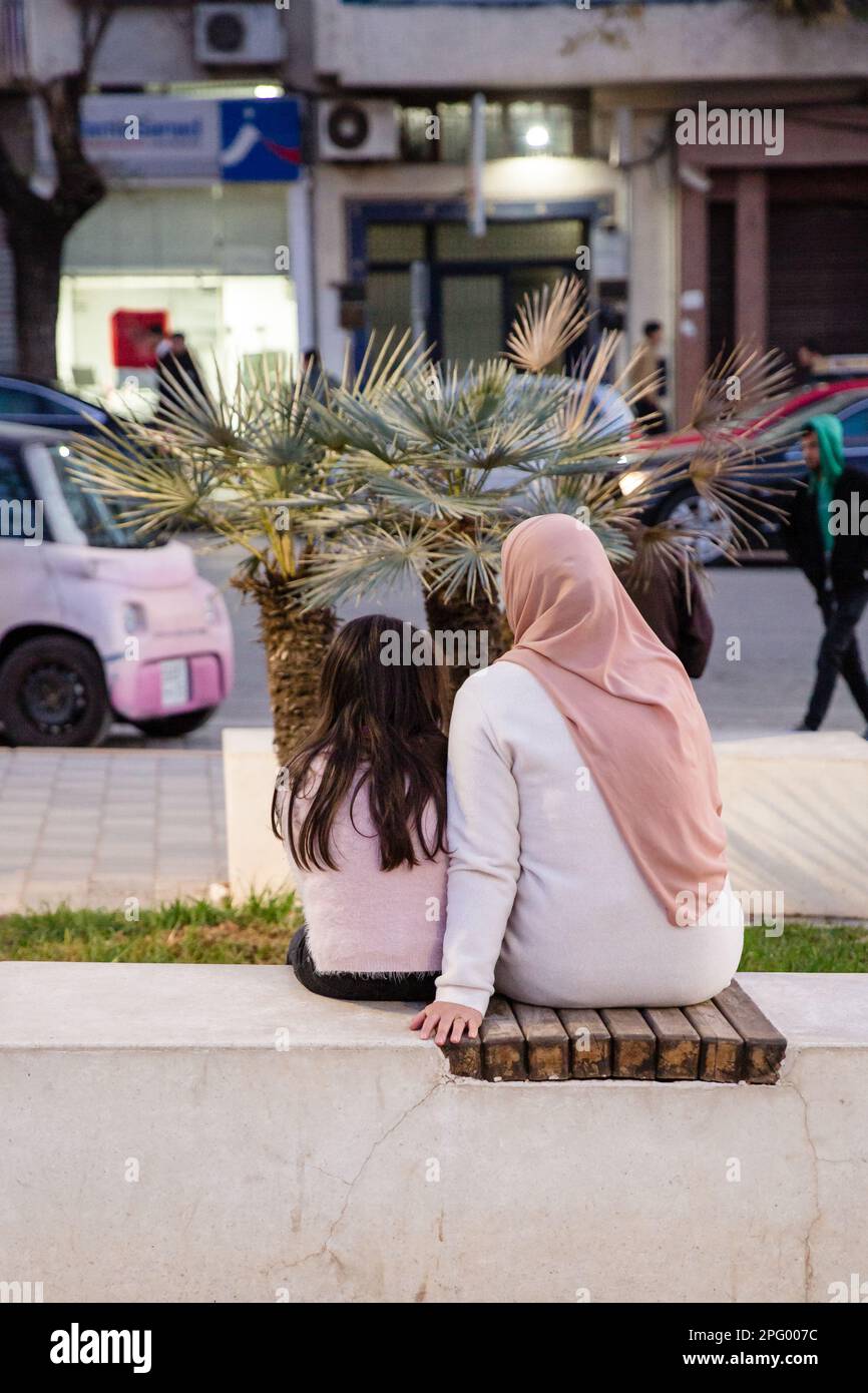 Vista da dietro di una donna e di una ragazza seduta a fianco di una strada a Fes Foto Stock
