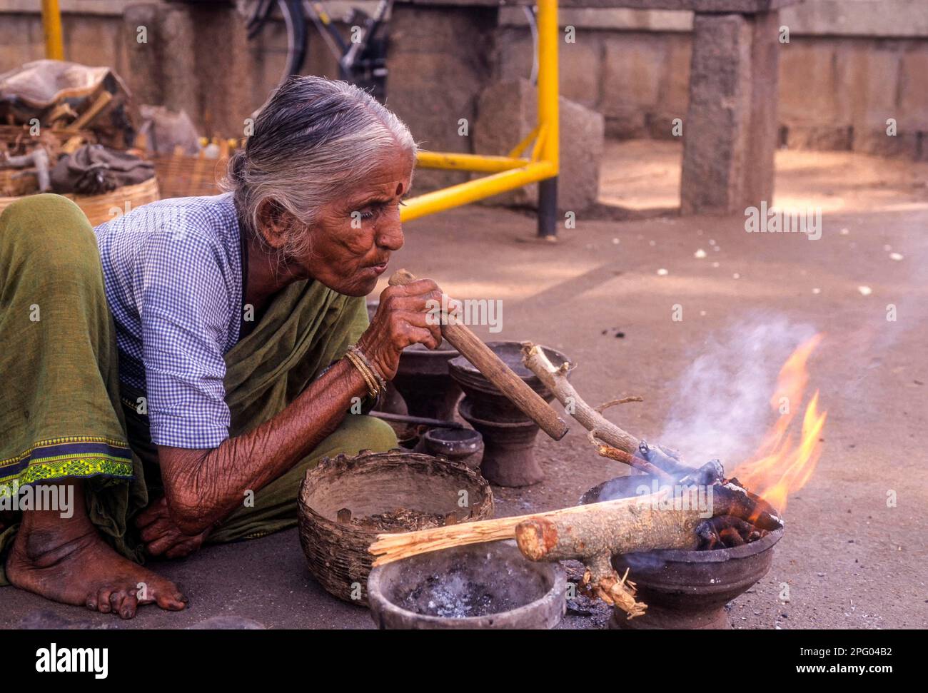 Una vecchia signora che brucia boschi utilizzando un tubo del vento a Kokkarebellur, Karnataka, India del Sud, India, Asia Foto Stock