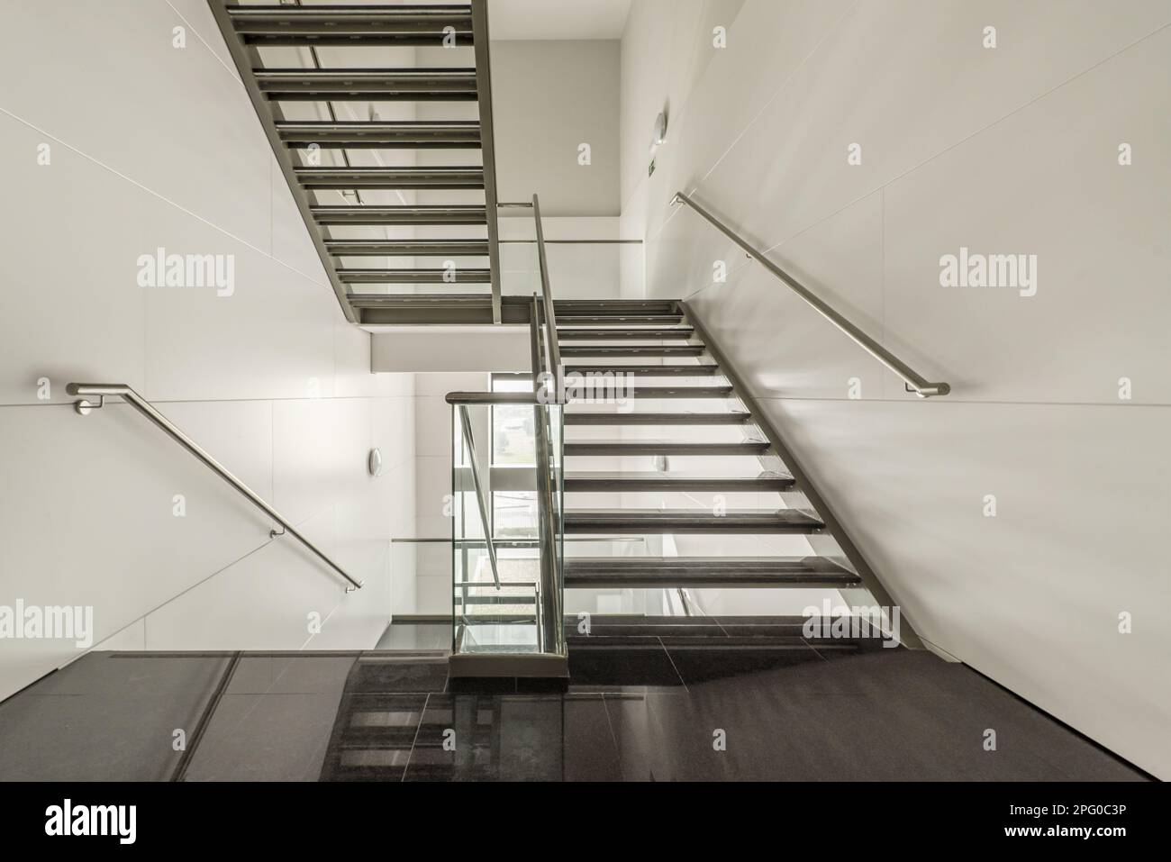 Scale dal design leggero realizzate in acciaio inossidabile, vetro temperato e gradini in granito nero lucido in un edificio di uffici Foto Stock